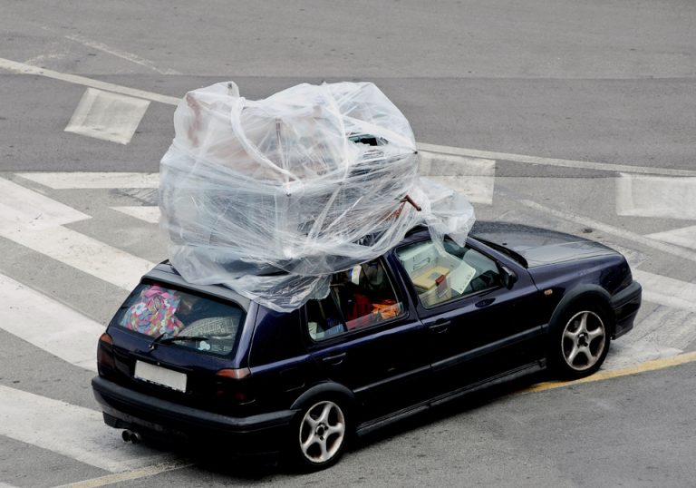 Vollgestopftes Auto mit Tüten, Kisten usw. Eingewickelte Möbel auf dem Dach. Als übertriebenes Bild für ein voll beladenes Auto zur Urlaubszeit