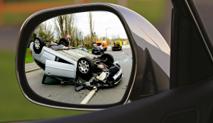 Fahrerflucht wird symbolisiert durch einen Blick in dem Außenspiegel, in dem der dahinter liegende Unfall zu sehen ist